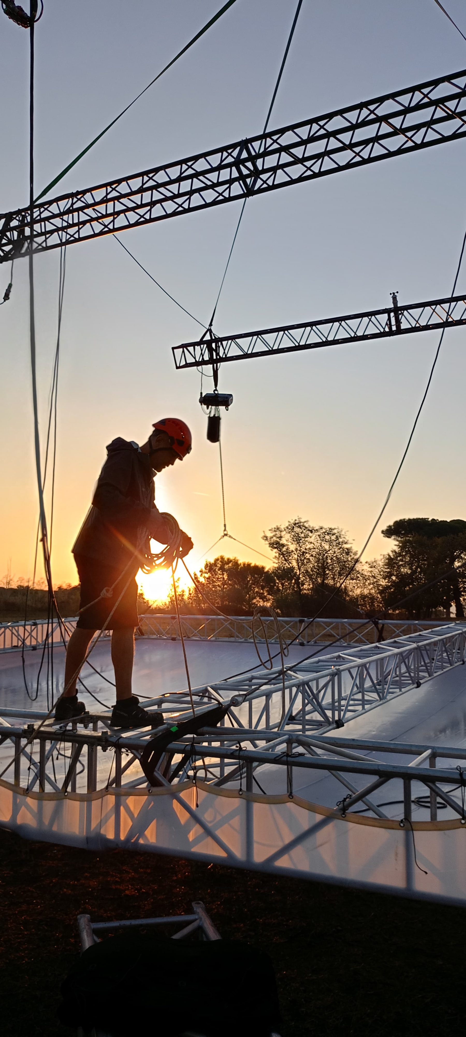 Rigger in quota in controluce al tramonto su una struttura.